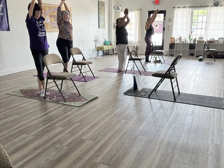 Members standing beside their chairs with arms raised overhead in a Love Seat Yoga class