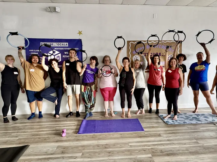 A class lined up on their mats holding Pilates rings overhead