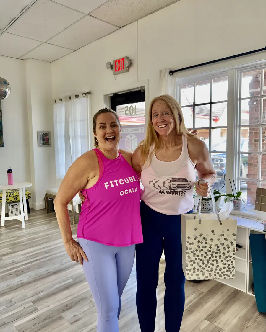 Two FitCube members laughing together in the studio, one in a FitCube Ocala tank
