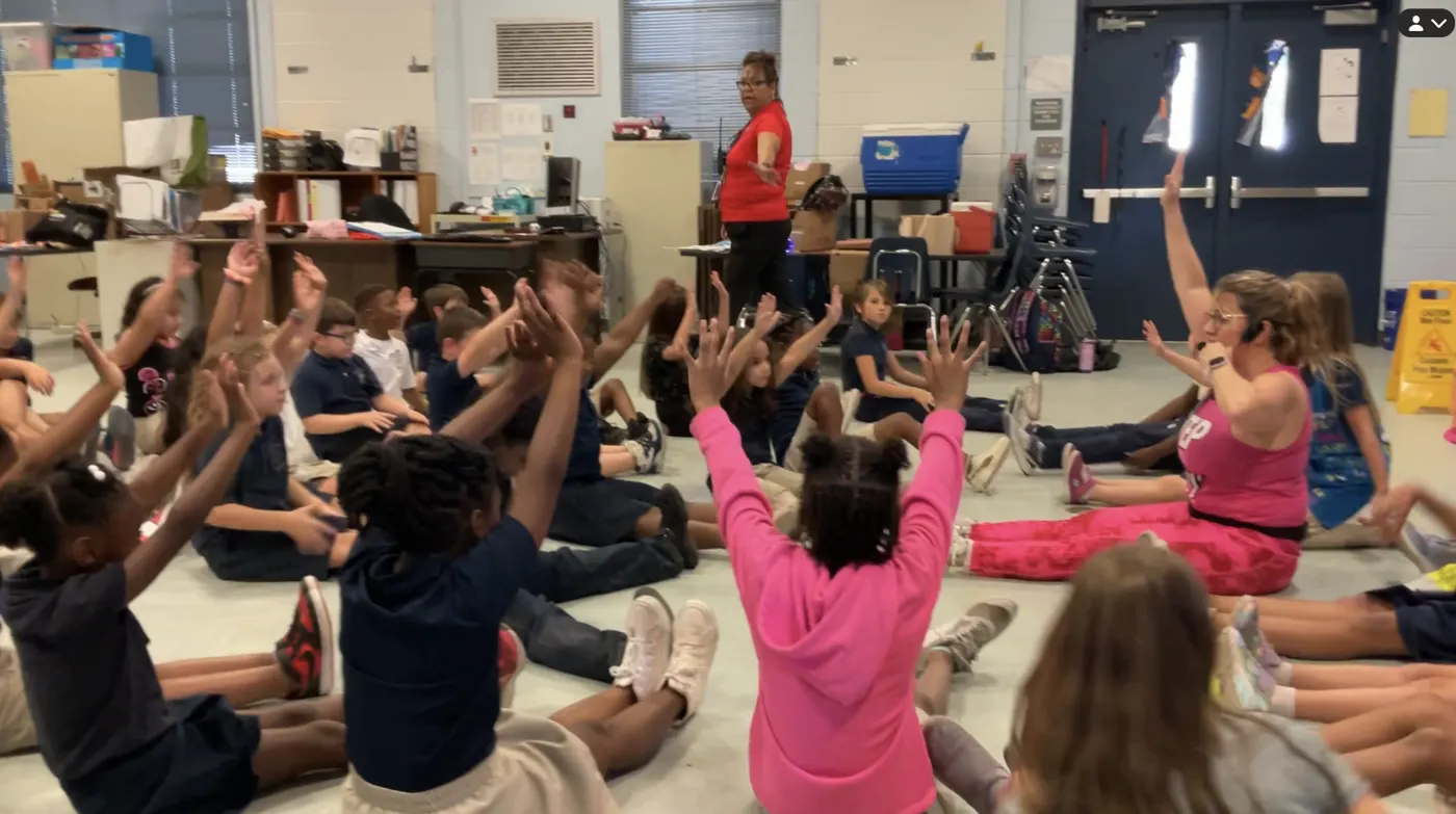 Elementary students reaching their arms up during a Zumba Kids class in a school classroom