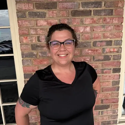 Alicia Askey smiling in a black tee in front of a brick wall